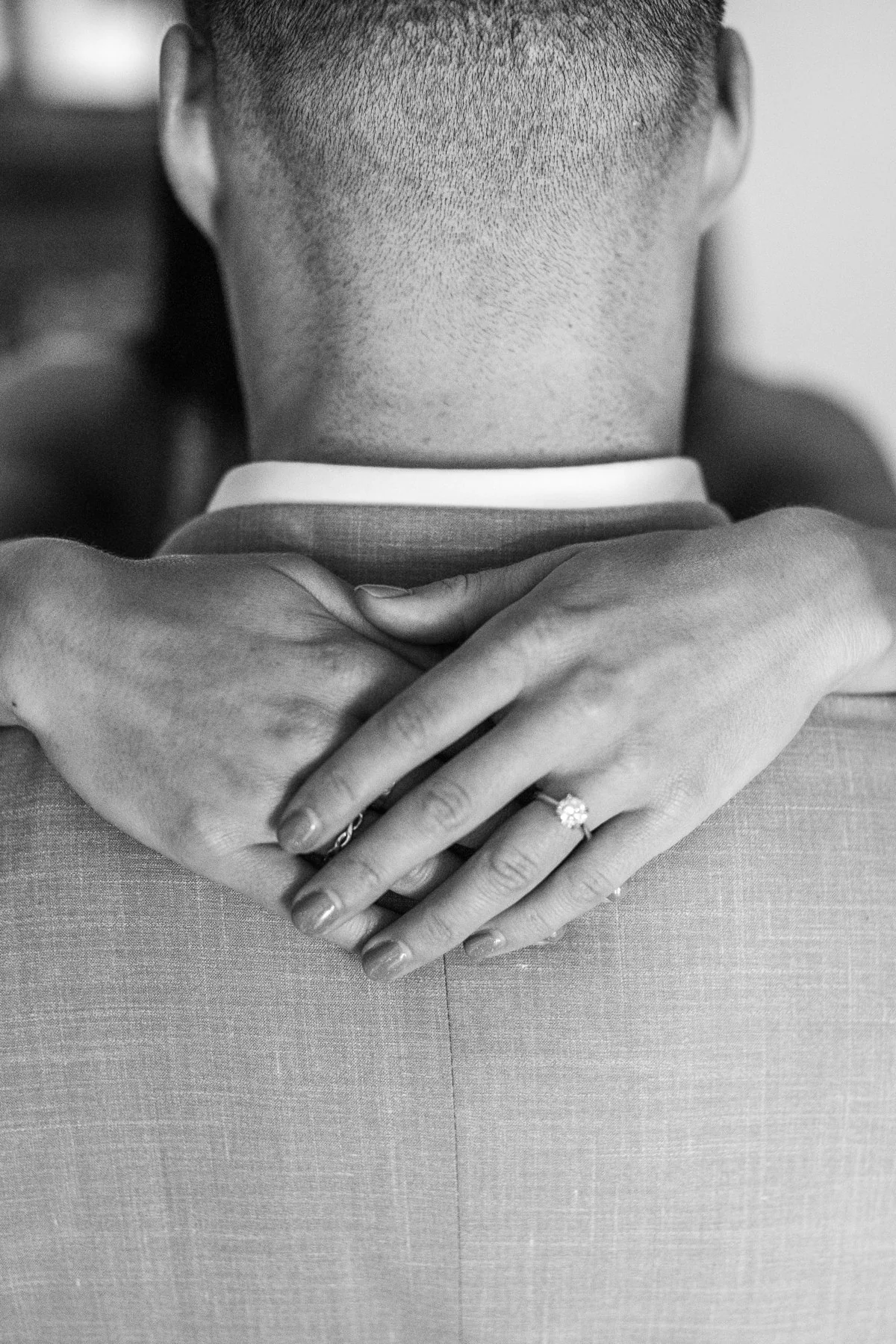 Black-and-white close-up of an engagement ring on a hand resting on a shoulder