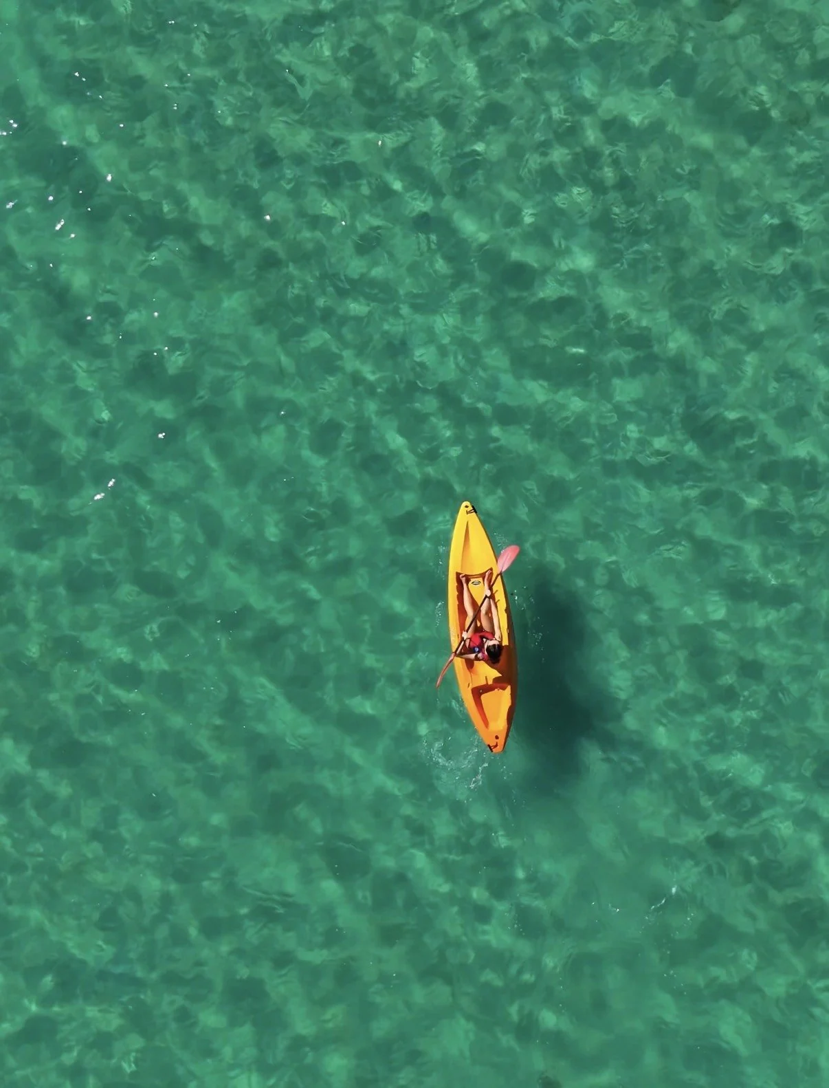 Overhead view of a yellow kayak on clear green water