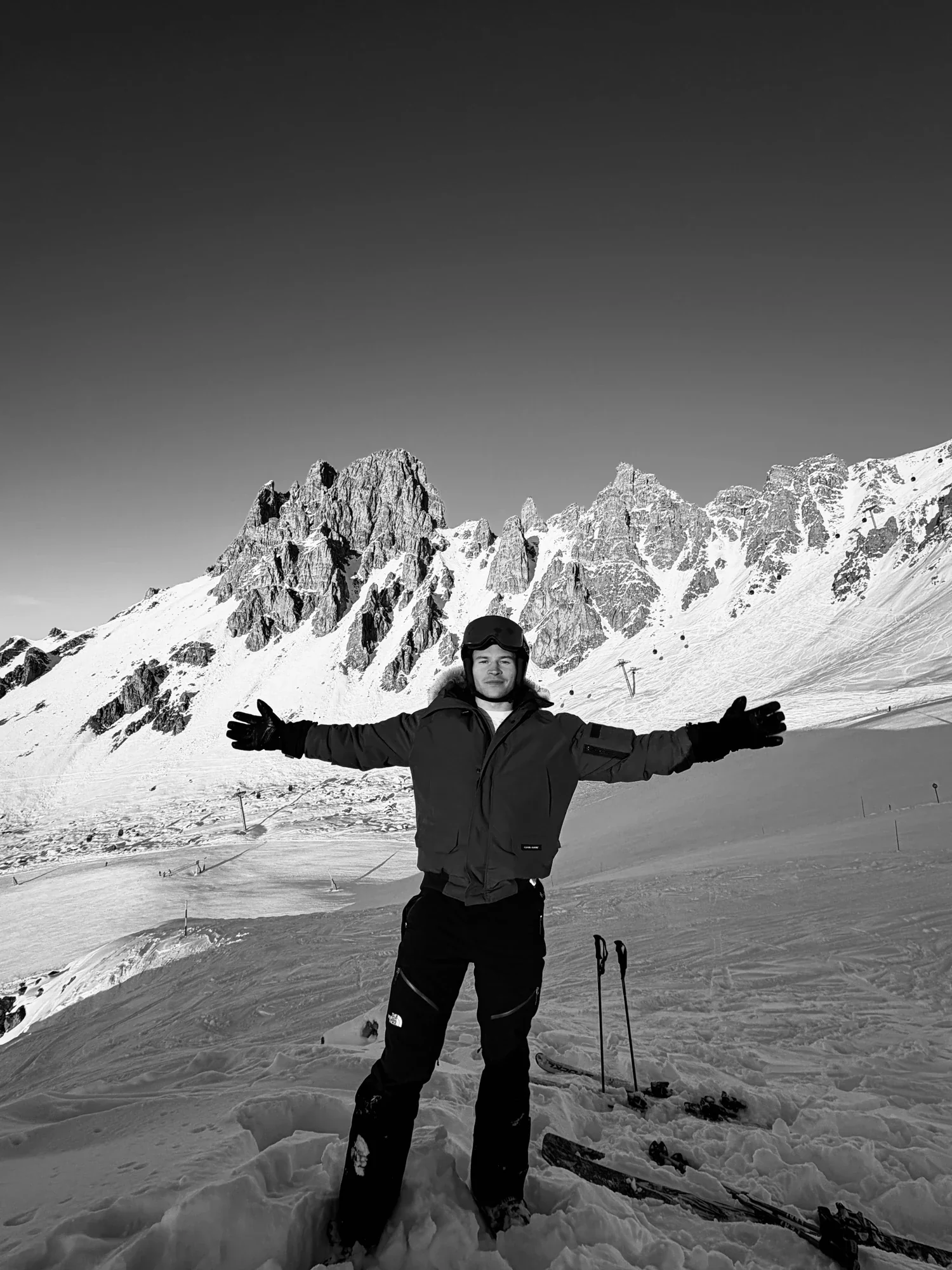 Murray Clark in ski kit with his arms outstretched beneath snowy peaks, in black and white