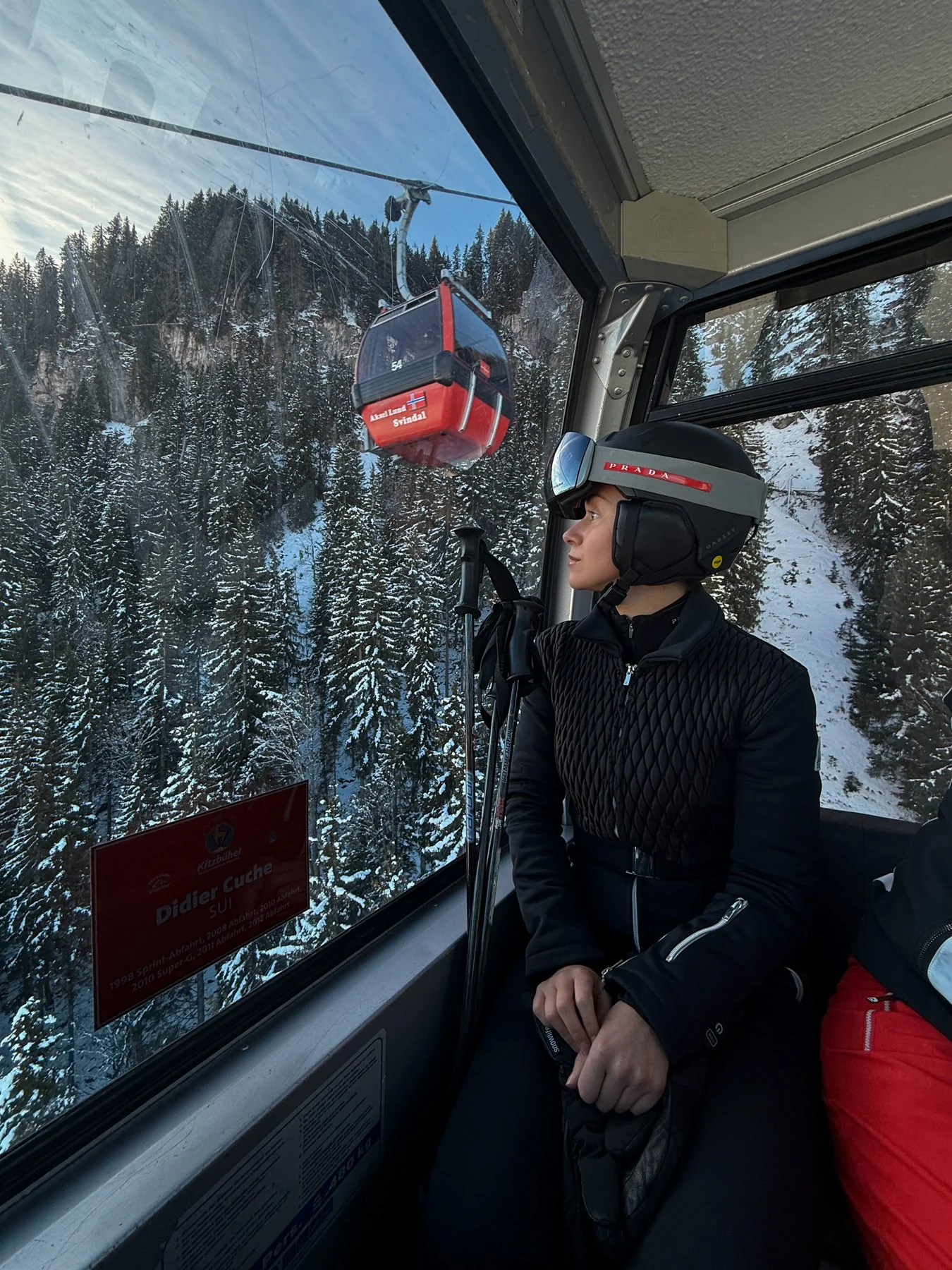 A skier riding a gondola above a snow-covered forest